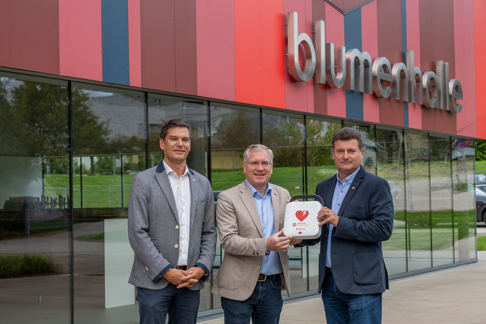 Defibrillator-Übergabe vor Blumenhalle in Steyr: Vizebürgermeister Gerald Nemeth und Stadtrat Markus Wieser übergeben Gerät an Bgm. Michael Feichtinger.