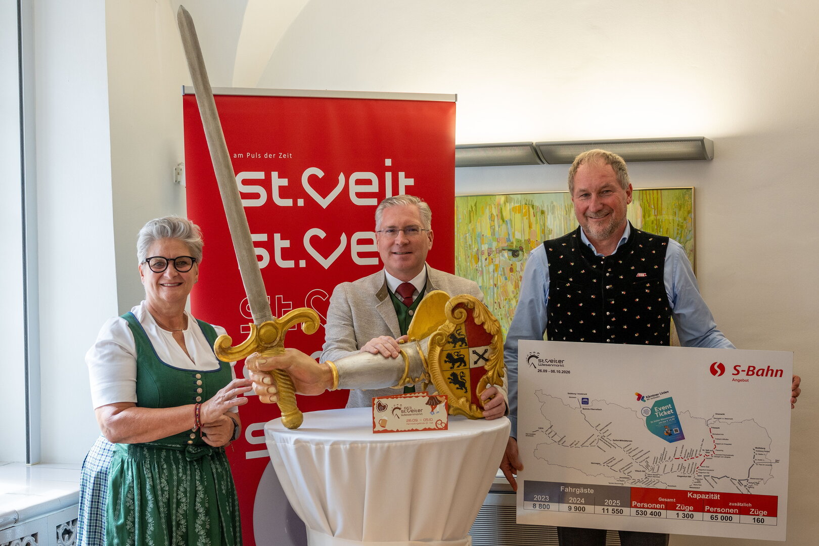 St. Veit: Bürgermeister Thomas Zwatz, Landeshauptmann-Stellvertreterin Gaby Schaunig und Landtagsabgeordneter Bgm. Gerhard Kofler mit Schwert und S-Bahn-Plakat