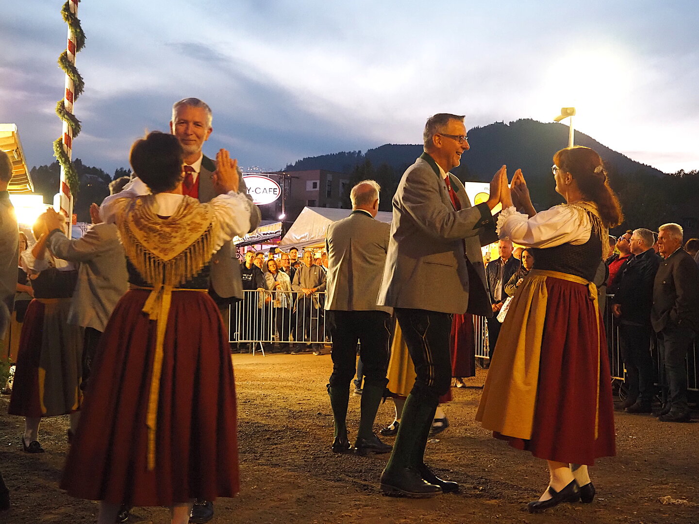 Paare tanzen in Tracht bei einem Volksfest im Abendlicht, Zuschauer im Hintergrund