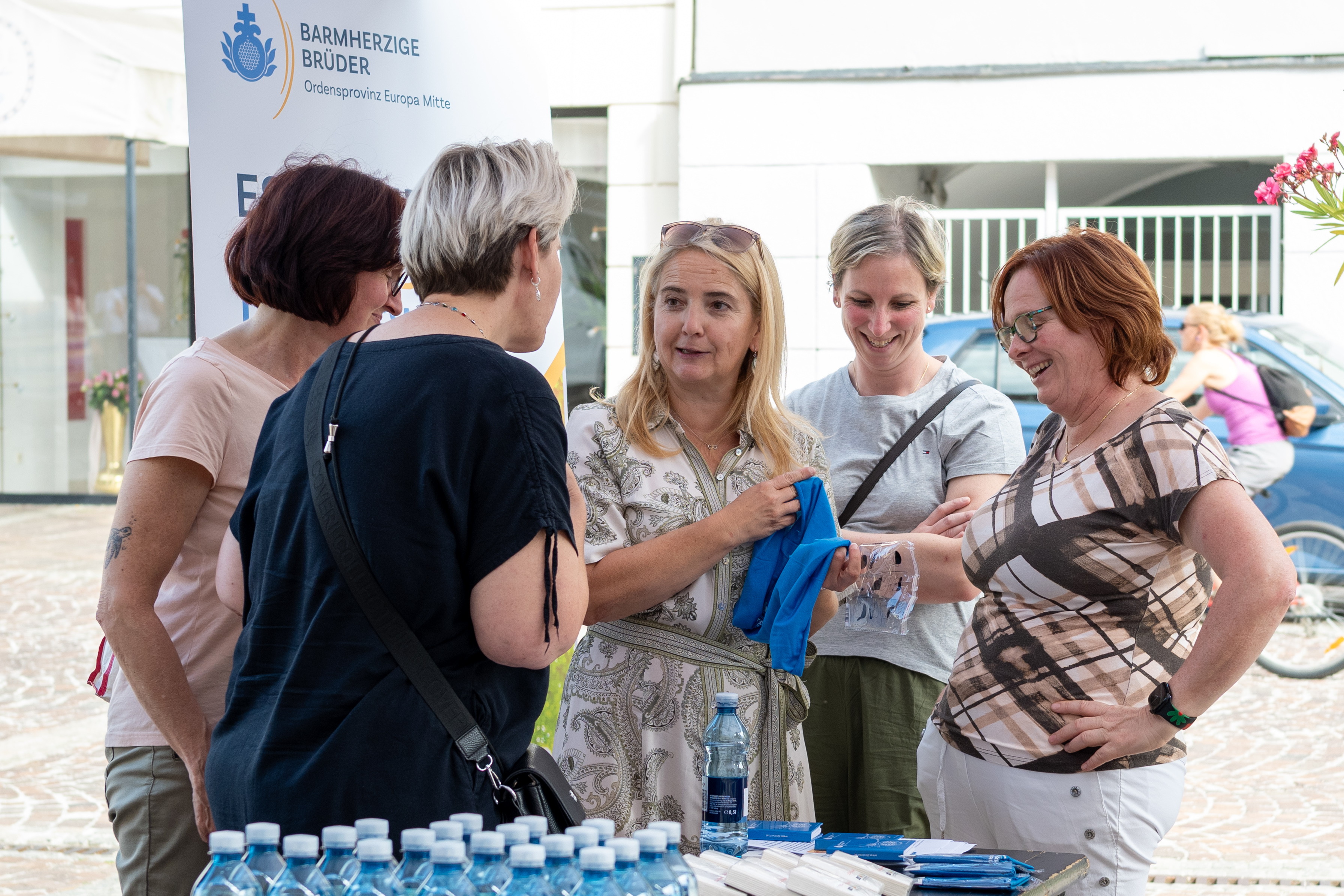 Frauen bei Informationsstand der Barmherzigen Brüder in Österreich, eine hält ein blaues Tuch.